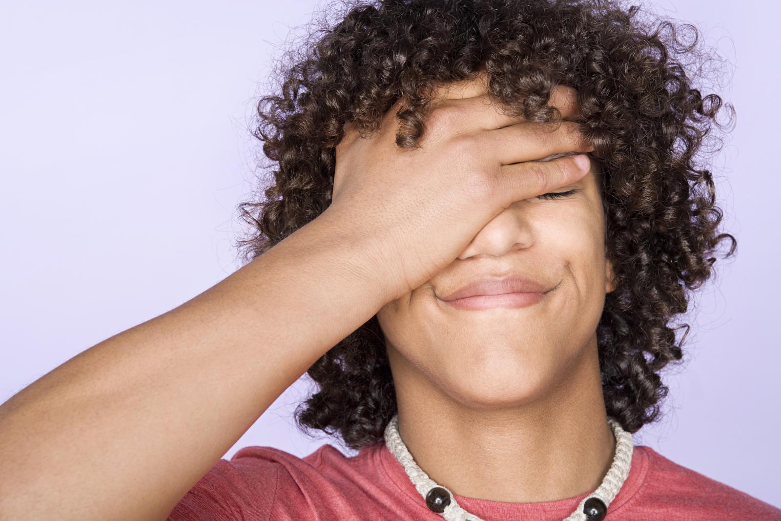 Teenage boy covering eyes with hand