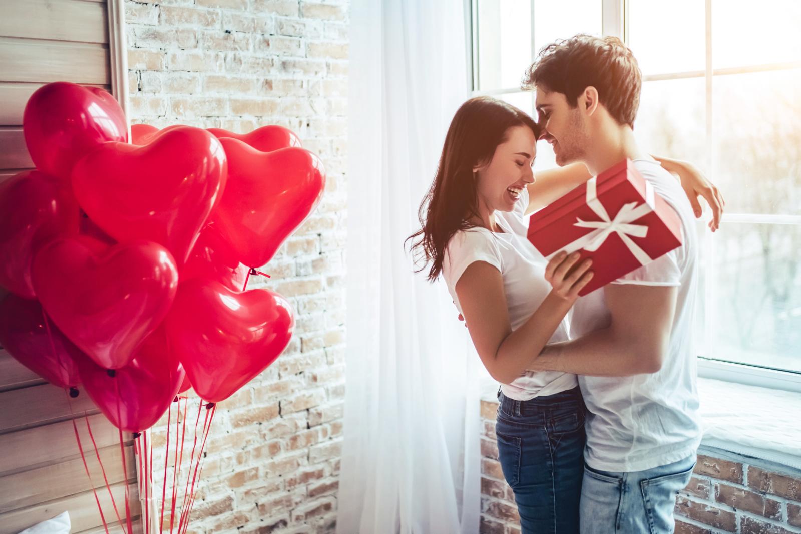 Celebrating Saint Valentine's Day with gift box in hand and air balloons in shape of heart