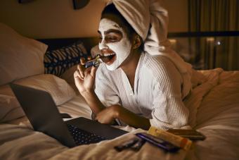 Woman relaxing at home using laptop and eating chocolate