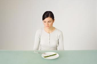 Young woman sitting in front of plate with single asparagus