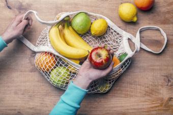 Reusable cotton mesh bag with fresh fruits and hand of man holding ripe apple