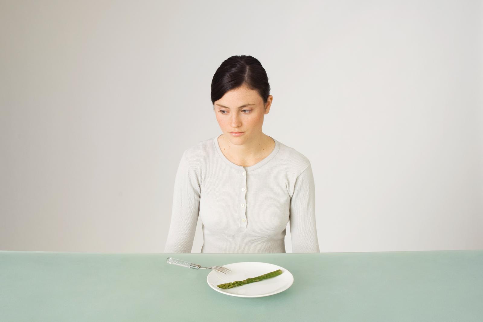 Young woman sitting in front of plate with single asparagus