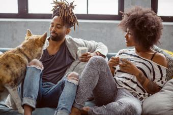 Young couple with dog sits on sofa drinking coffee 