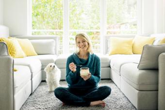 Happy woman with dog eating fruit yoghurt in living room