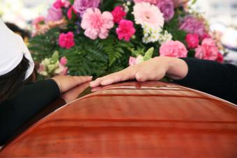 A hand on a casket and flowers in the background