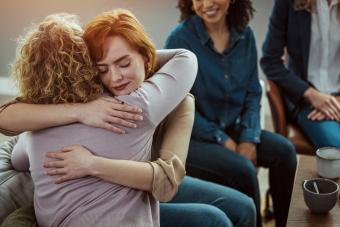 Young woman receives a hug from the woman sitting next to her during group therapy