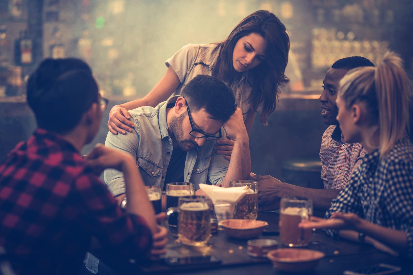 Group of friends consoling their friend who is sitting displeased in a bar