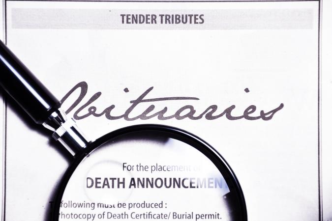 Magnifying glass and obituaries advertisement on newspaper.