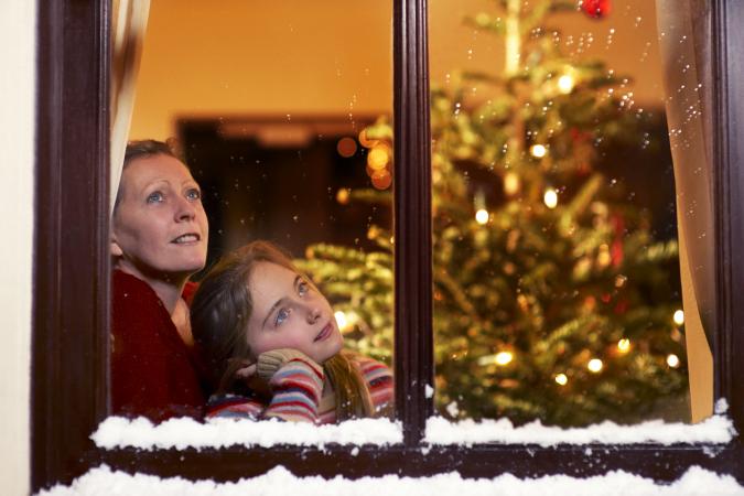 Girl and mother gazing out of window at christmas