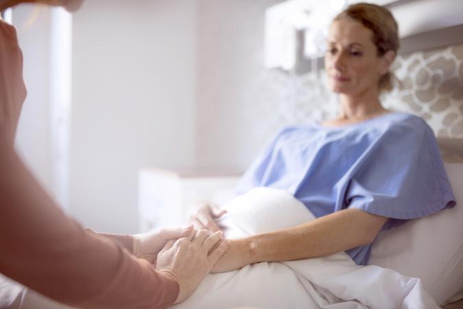 Woman consoling sister in bed at hospital ward