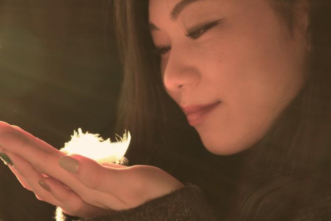 Woman holding white feather cupped between her hands