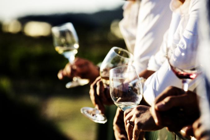 People holding glasses of wine to pour one out