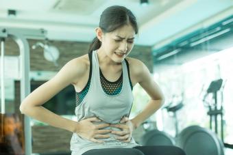 mujer siente dolor en el estómago mientras hace ejercicio