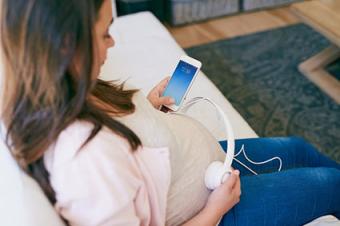 Mujer que usa los auriculares sobre su vientre embarazado
