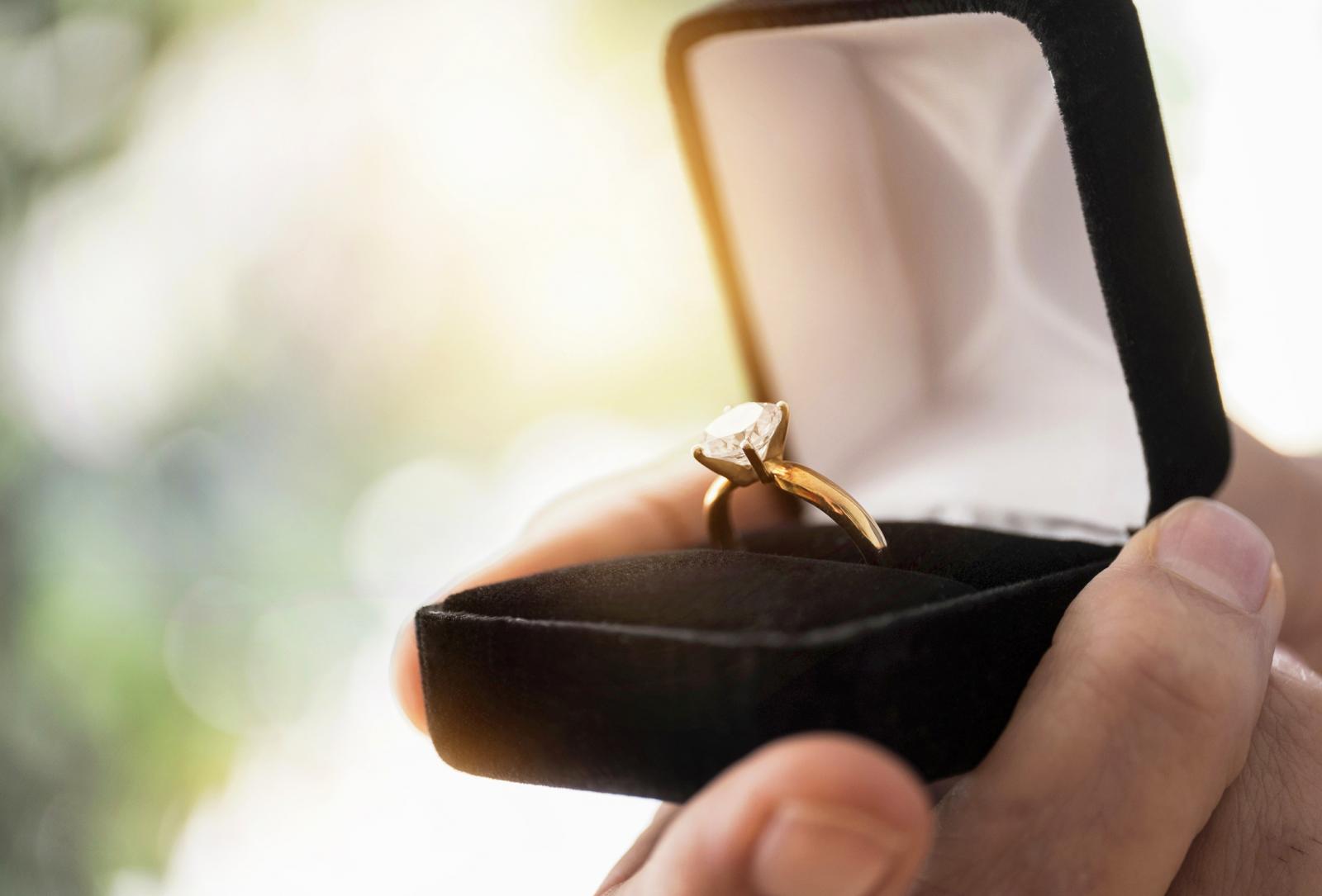 Mans hand holding open box with engagement ring
