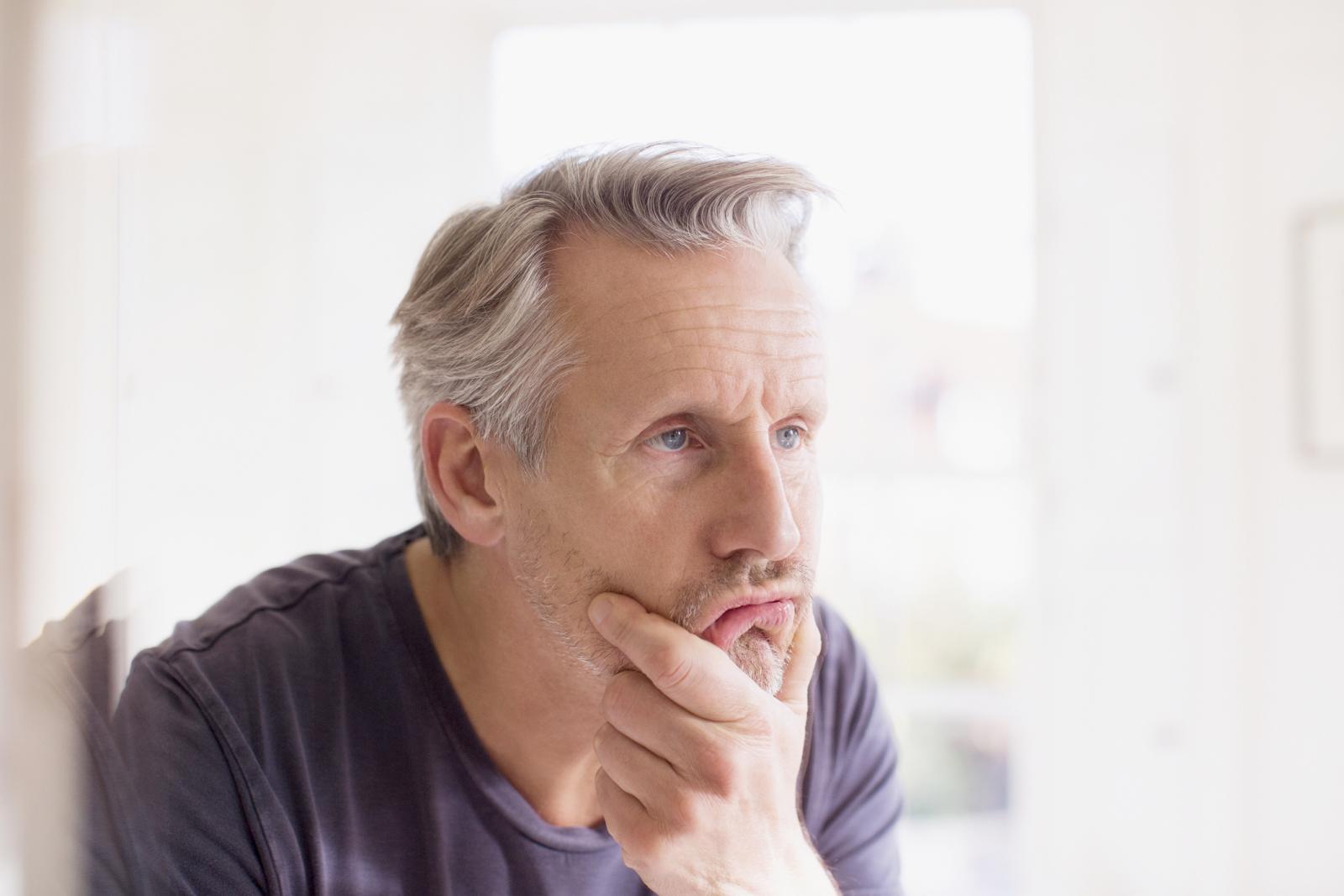 Mature man touching face in bathroom mirror