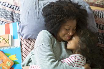 Smiling mother and daughter hugging on bed