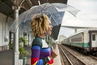 Cheerful young woman enjoying while standing with umbrella at railroad station while raining