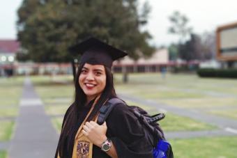 Smiling Woman In Graduation Gown Standing On Field Campus