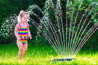 toddler girl running in water sprinkler