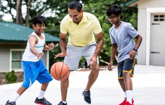 father and two sons playing basketball in driveway of home