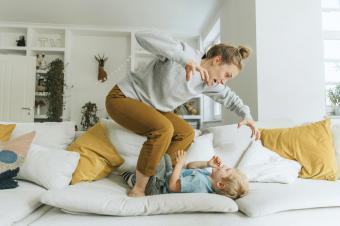 Mother gesturing while standing on sofa by boy at home