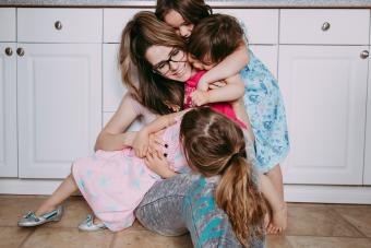 Mother sitting on the floor in her kitchen surrounded by her 3 daughters