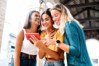 Three happy friends watching a smart phone mobile outdoors 