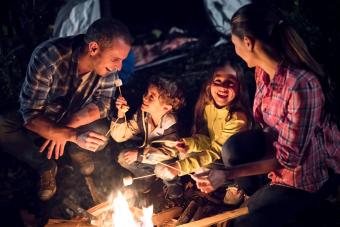 Family outdoors sitting by a bonfire eating marshmallows