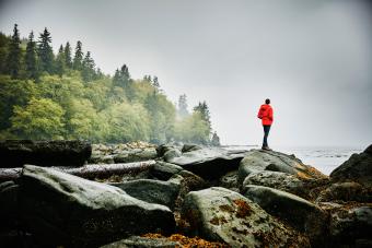 Man standing on boulders on shoreline of ocean