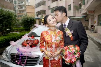 Groom kissing bride on cheek in front of car