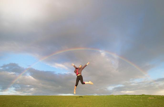 woman jumping in air celebrating feng shui good luck underneath a rainbos in the sky