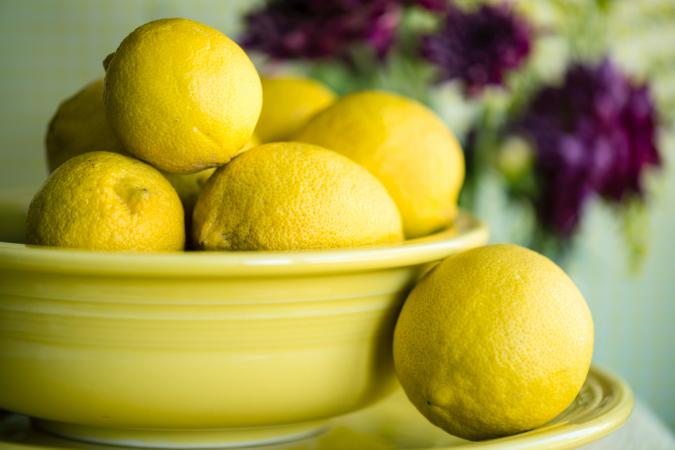 Lemons In Bowl On Plate With Flowers Behind