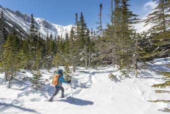 A young woman hiking on a sunny, snowy winter day in the White Mountains of New Hampshire