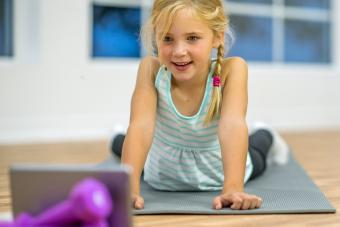 An elementary age girl is doing yoga on an exercise mat