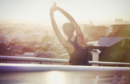 Female runner stretching arms on urban footbridge at sunrise