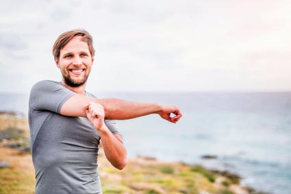 Happy sporty young man stretching on the coastline