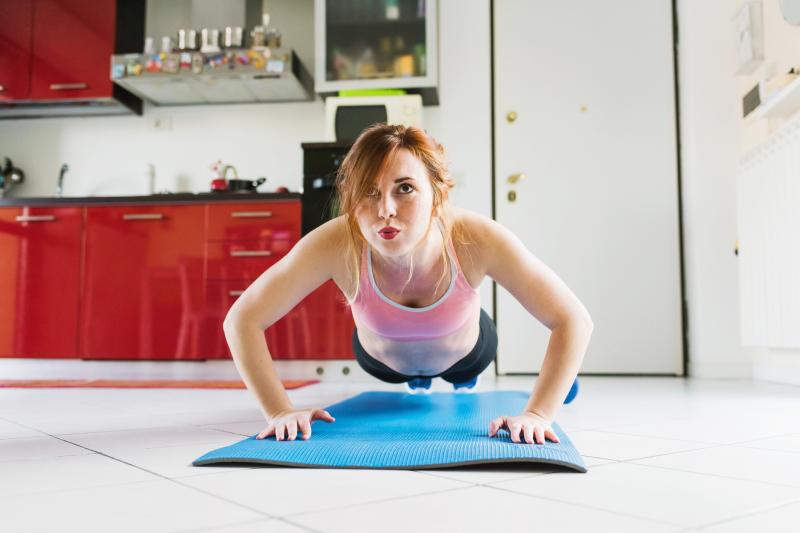 Young woman doing push ups on kitchen floor