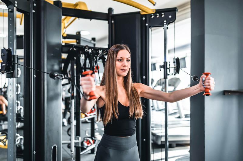 Young fit woman doing exercise in a crossover exercise machine
