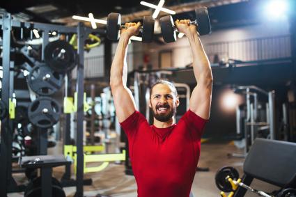 Young man lifting up dumbbells at the gym