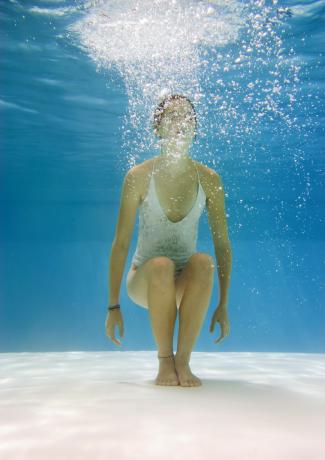 Teenage girl in pool doing the chair pose under water