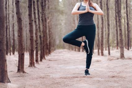 Woman Practicing Yoga In Tree Pose At Forest