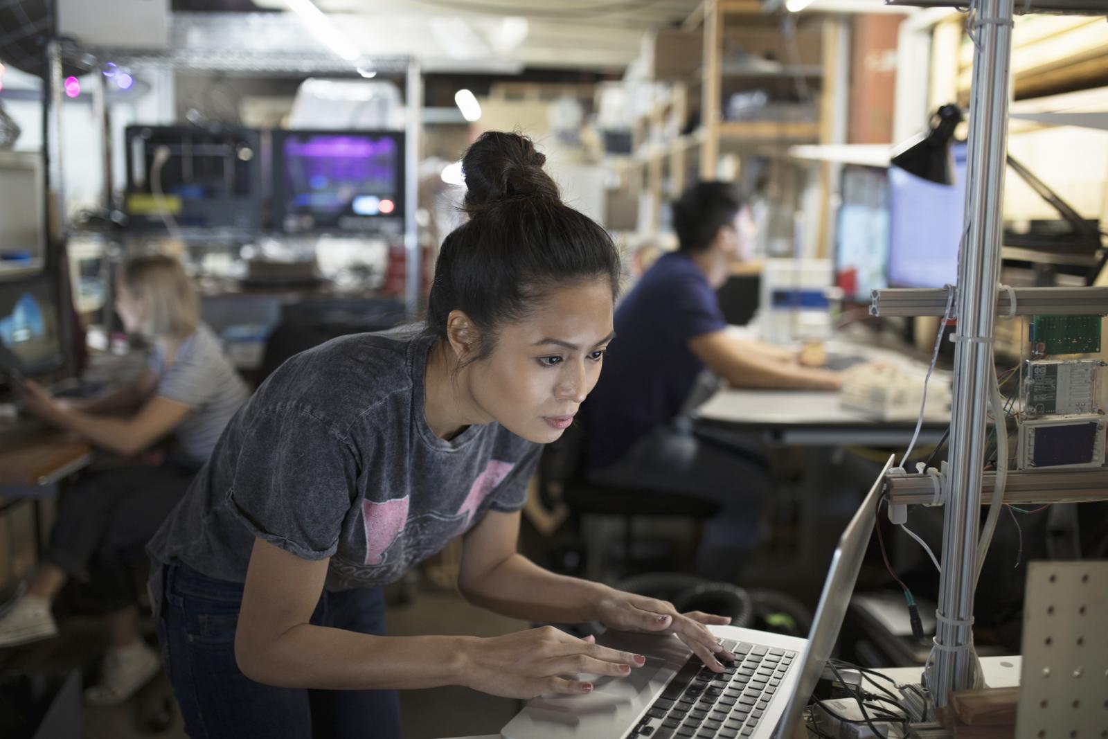 Focused female engineer working at laptop in workshop