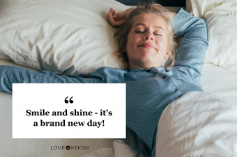 Smiling young woman stretching her arms in bed on a sunny morning