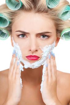 Frowning woman in curlers lathering face