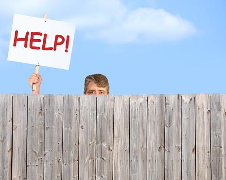 Man with HELP sign looking over fence