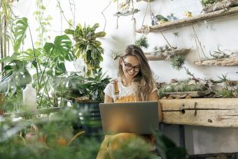 Happy young woman using laptop in a small gardening shop