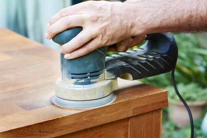 Man sanding an oak table with a random orbital sander