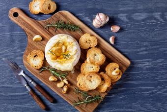Brie cheese baked in the oven with rosemary sprigs, garlic cloves, served with croutons