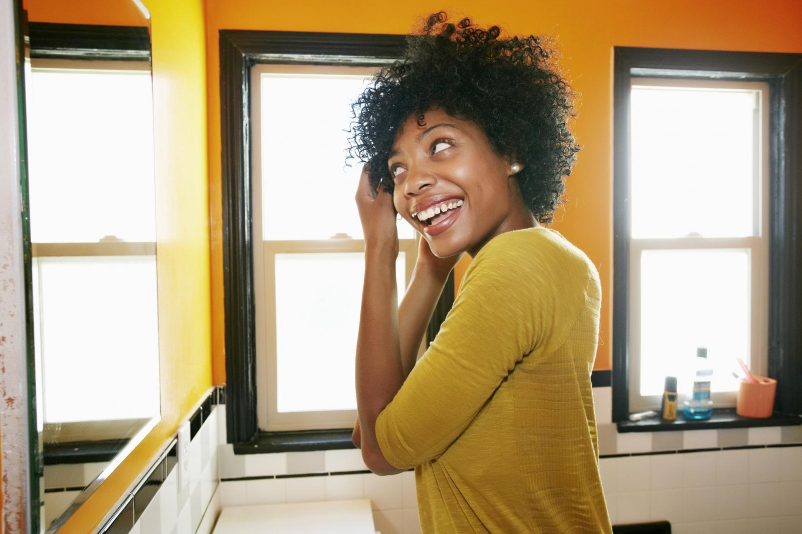 African American woman styling hair in bathroom mirror